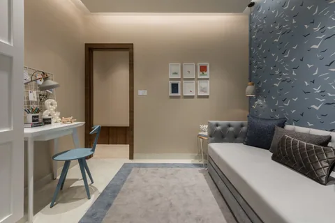 A compact child’s room in a Mumbai two-bedroom show apartment with a grey daybed, a fitted study desk and white wardrobe storage