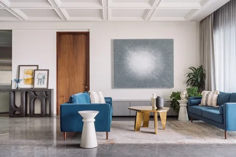 A South Mumbai apartment living room with blue armchairs, a stone side table, grey upholstery and a timber door