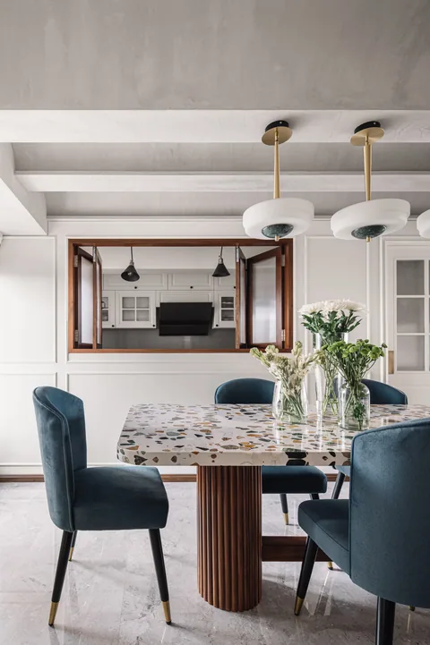 A Mumbai apartment dining room with blue upholstered chairs, a timber table and hanging brass lights