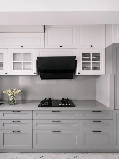 A fitted Indian apartment kitchen in Mumbai with grey cabinets, white upper storage, a hob and chimney
