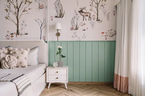 A child’s bedroom in a Mumbai apartment with mint-green panelling, illustrated wallpaper, a white bed and timber flooring