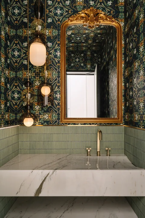 A Mumbai apartment powder room with green tiles, patterned wallpaper, an ornate brass mirror and a pale basin