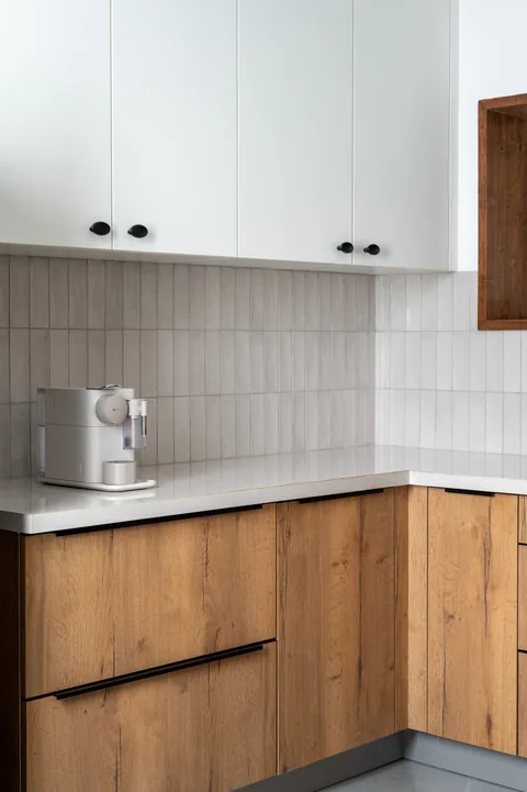 A compact Mumbai apartment kitchen with timber base cabinets, white upper cabinets and a pale countertop